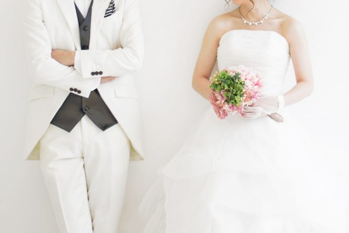 画像：腕を組んだ白いタキシードの新郎とウエディングドレスの新婦