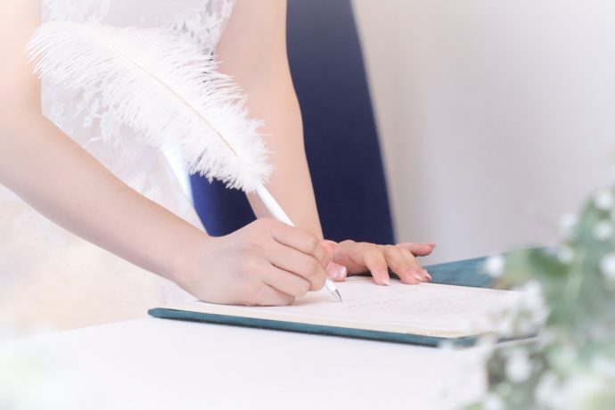 羽ペンで結婚証明書にサインする花嫁の手元