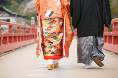 太鼓橋を渡る色打掛を着た新婦と紋付袴を着た新郎の後ろ姿の写真