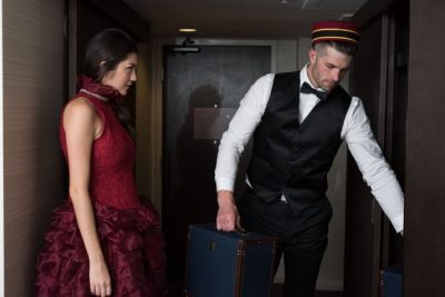 トランクを部屋に運び入れるベルマンと赤いドレスの女性の写真
