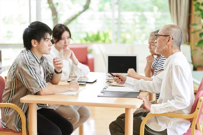 テーブルを囲む険悪な雰囲気の若い夫婦と老夫婦の写真