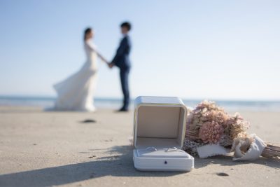海辺で手をつなぎ向かい合う花嫁と花婿の手前にある花束と指輪にピントが合った写真