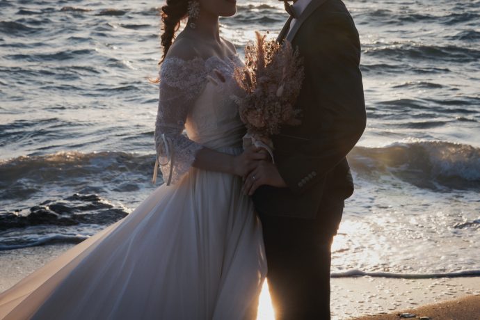 海辺で向き合い体を寄せる花嫁と花婿の写真