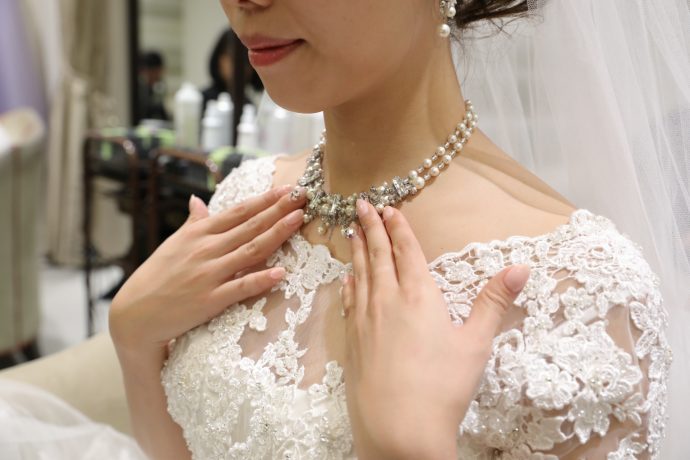 首元に手をやるダイヤのネックレスをした花嫁の写真