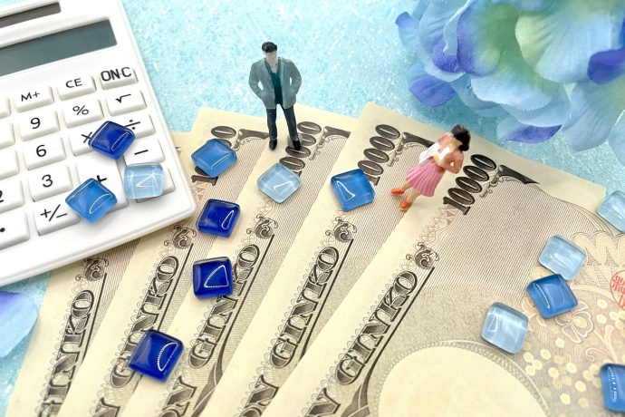 １万円札の上に立つ男女のフィギュアと電卓と青い花、青いタイルの写真