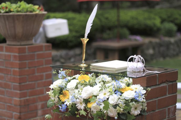 レンガ調のガーデンに設置された装花と結婚証明書と羽ペンとリングピローが置かれた台