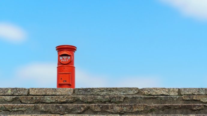 石壁の上に立つ青空をバックにした赤い郵便ポスト