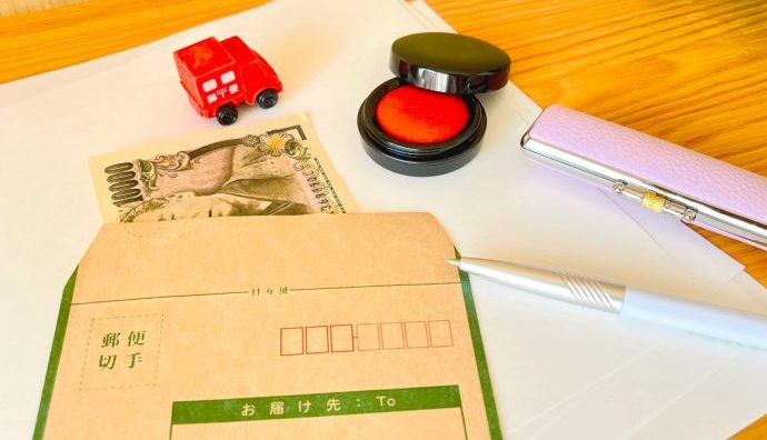 現金書留の封筒と印鑑、1万円札、郵便カーのおもちゃ