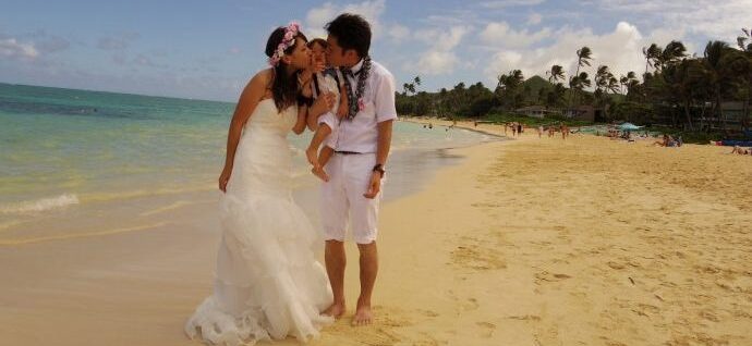 沖縄のビーチで両側から我が子にキスをする新郎新婦