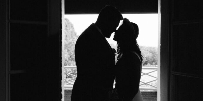 画像：ドアの前で鼻先をくっつけ合う花嫁と花婿のシルエット