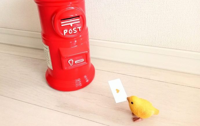 赤いポストのおもちゃと手紙を咥えた小さな黄色い鳥