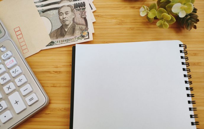 ノートと電卓、3万円札を広げた机の写真