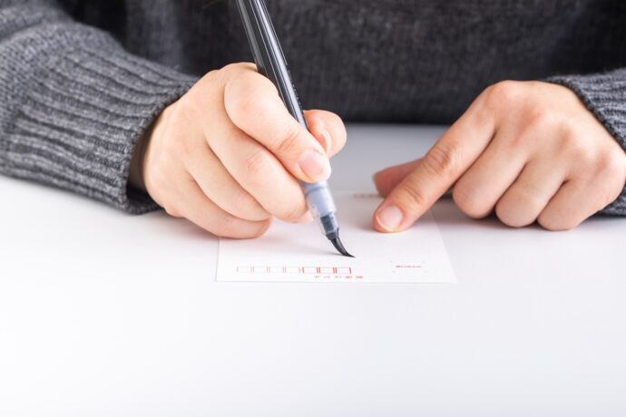 画像：筆ペンを持ちハガキの宛名を書いている手元