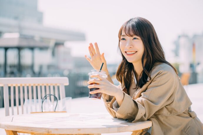 画像：コートを着てテーブルに着き誰かに手を振る女性