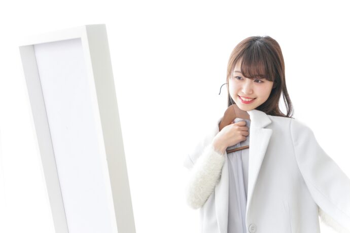画像：鏡の前で白いコートを試す女性