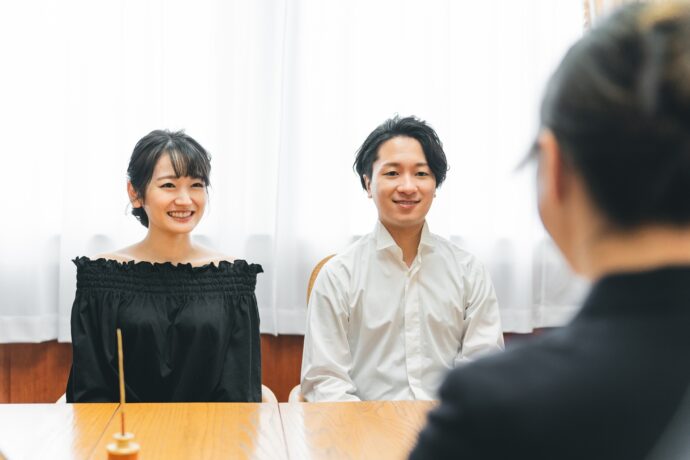 画像：並んでソファに座る男女二人とテーブルをはさんで対峙している