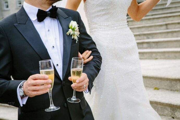 画像：シャンパングラスを2つ持つタキシードの男性とウエディングドレスを着た女性が大階段で並び立っている