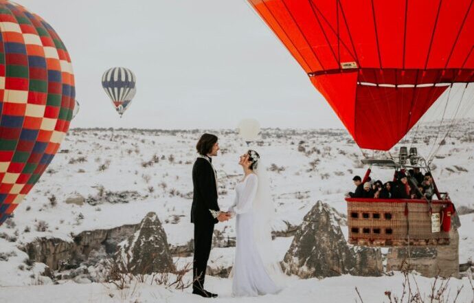 画像：雪の上で気球を背景にウエディングフォトを撮る花嫁と花婿
