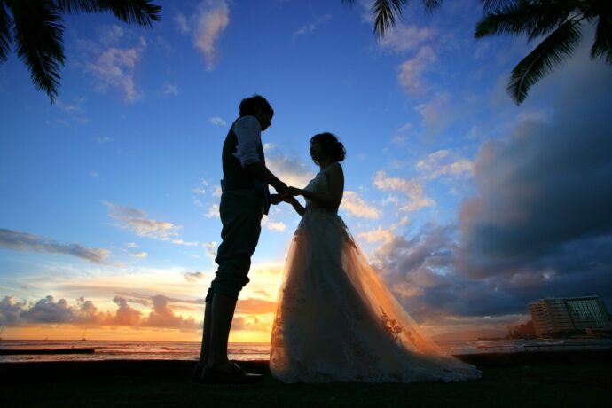 画像：夕焼けのグラデーションになった空を背景に手を取り合うカップルのシルエット