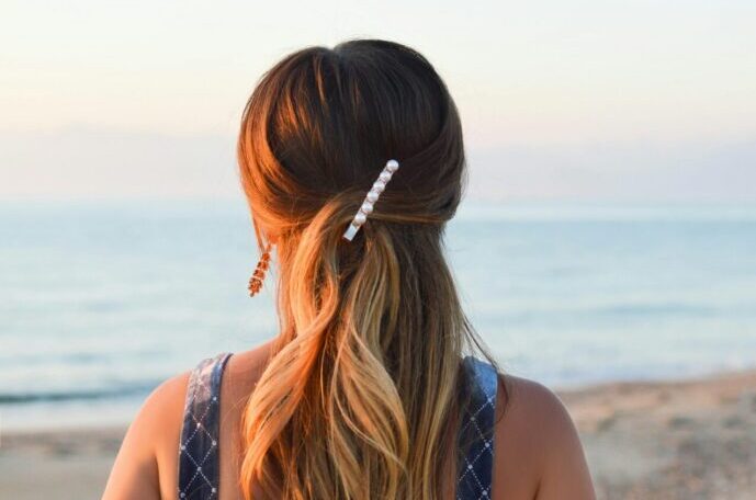 画像：海を背に立つ、パールのバレッタで髪を留めた女性の後ろ姿
