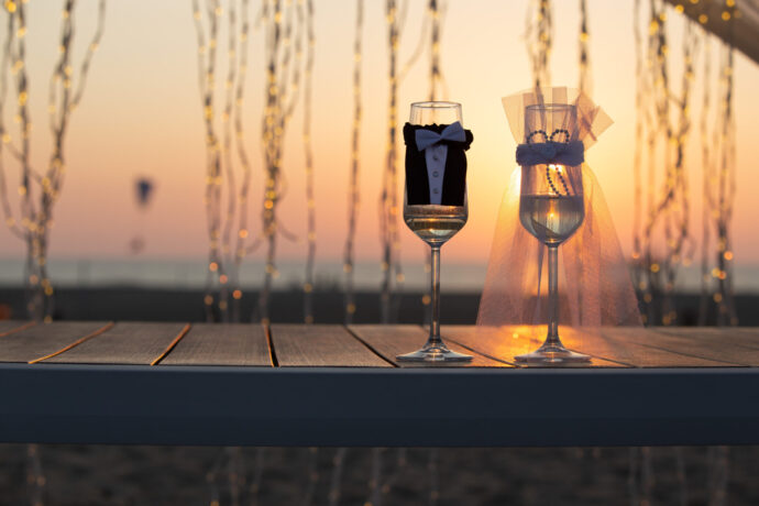 画像：夕日に照らされるタキシードとウエディングドレスの装飾がなされたフルートグラス