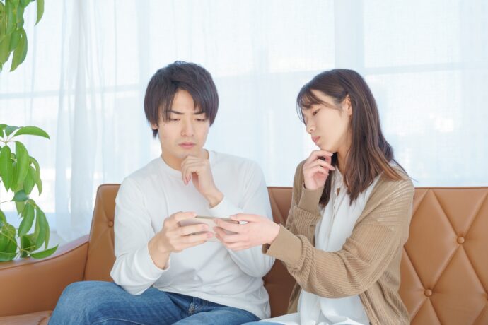 画像：スマホを覗き込み悩む若い男女