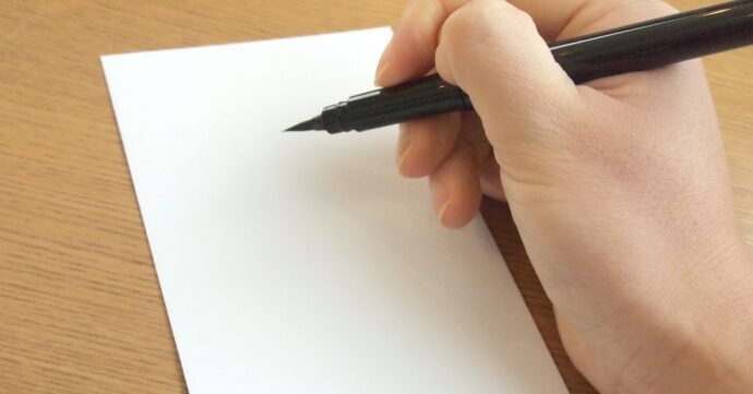 画像：筆ペンを持ち白い封筒に宛名を書こうとしている右手