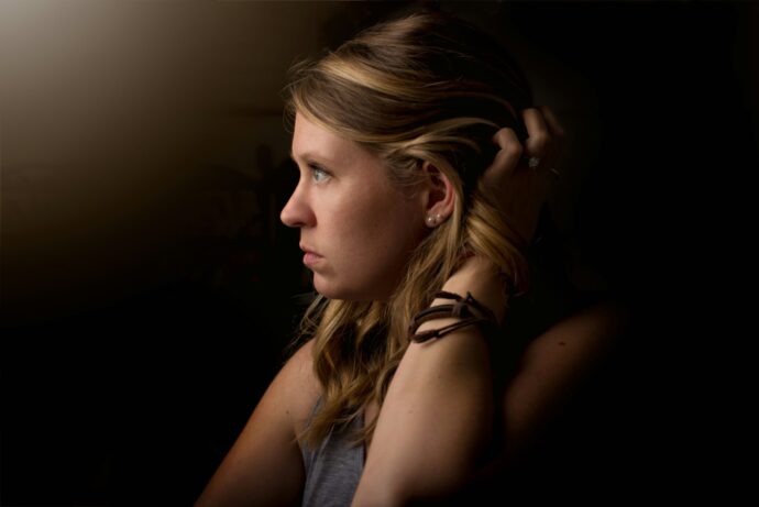 画像：暗がりで両耳あたりの髪を掴み遠くを見据える女性