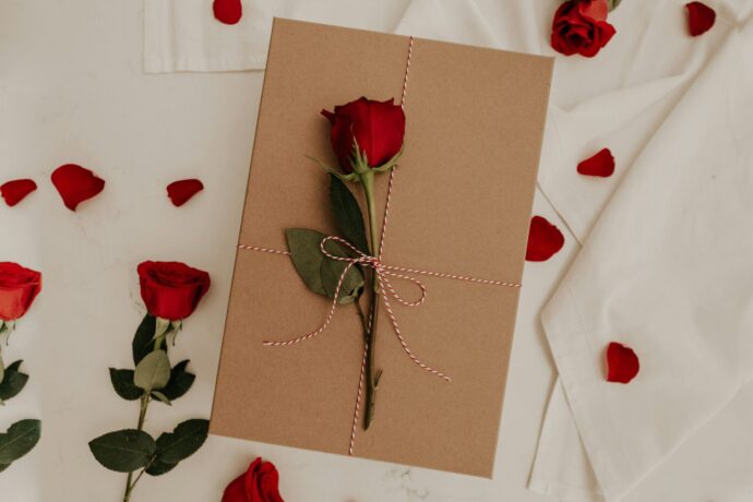 画像：クラフト紙に包まれたプレゼントと上に置かれたバラ、周りに散らばるバラの花弁