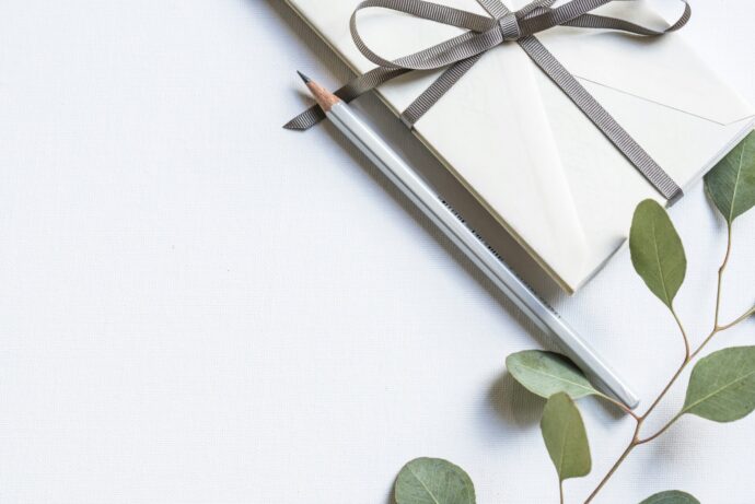 画像：白い机の上のグレーのリボンがかかった白いプレゼントと鉛筆と観葉植物