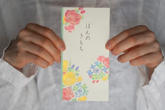 画像：ほんのきもちと書かれた封筒を両手で持っている胸元のアップ