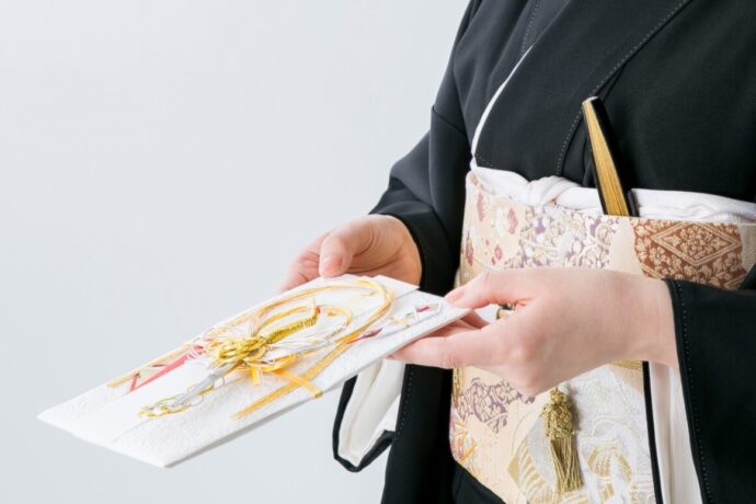 画像：黒留袖を着て豪華なご祝儀袋を差し出す女性
