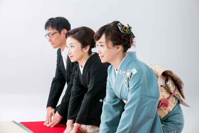 画像：赤い絨毯の上で三つ指を着く正装した親子三人
