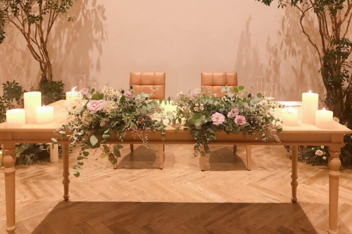 画像：クロスのかかっていないテーブルとイス、キャンドルとグリーンの装花実例