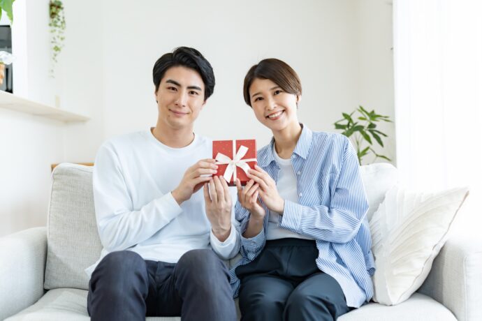 画像：ソファに座りプレゼントを二人で持つ男女