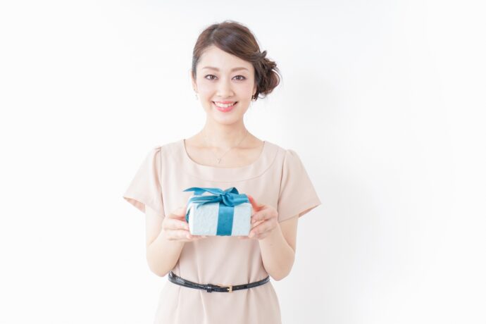 画像：ブルーのリボンがかかったプレゼントボックスを差し出すワンピースの女性