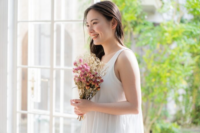 画像：白いワンピースを着て花束を持つ女性