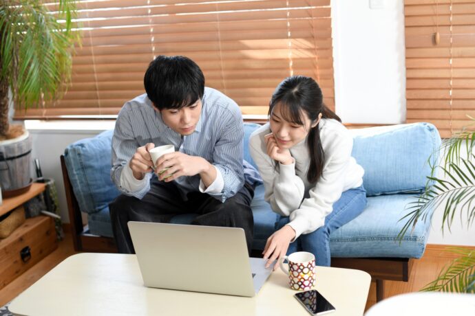 画像：リビングでパソコンを覗き込む若い男女