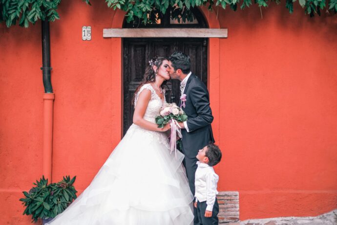 画像：赤い壁の前でキスをする新郎新婦