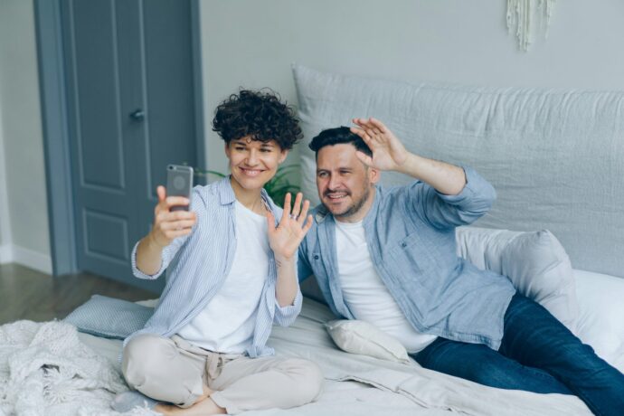 画像：スマホに向けて笑顔と手を向ける男性カップル