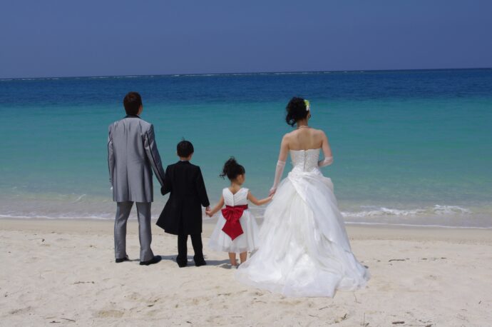 画像：子どもたちと手を繋ぎ海辺に立つ夫婦