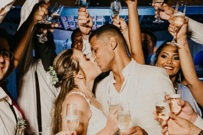 画像：友人たちとの騒々しいパーティーの中キスを交わす新郎新婦