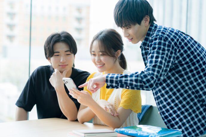 画像：スマホを覗き込む若い男女3人