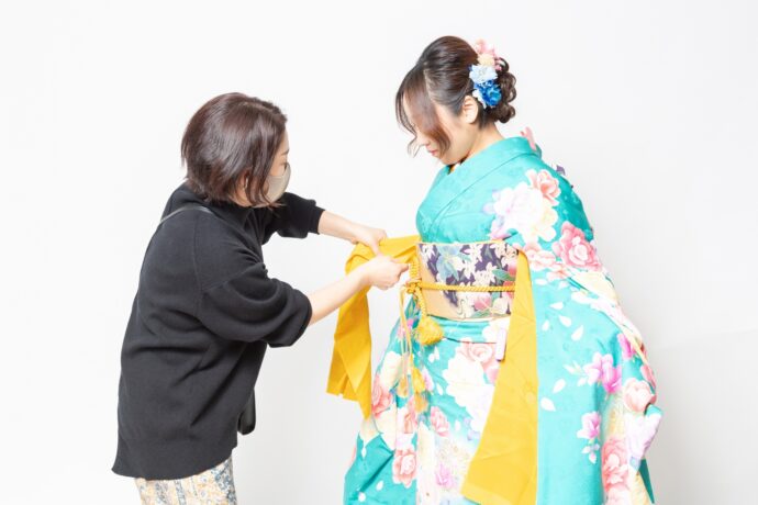 画像：着付け師と振袖を着つけられている女性