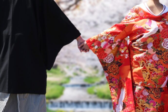 画像：桜の前で手を繋ぐ和装の新郎新婦