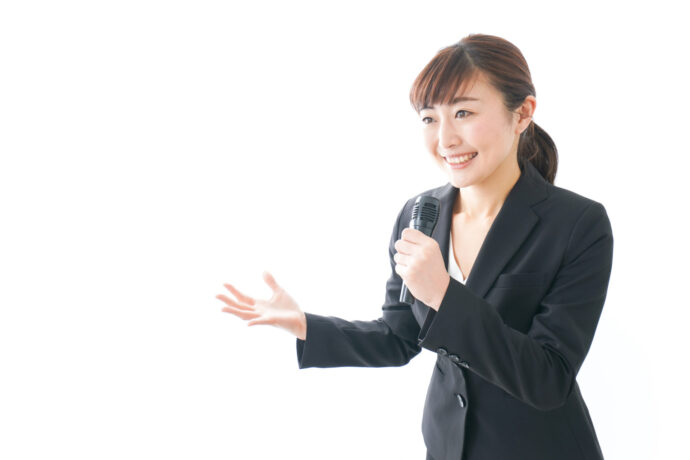 画像：スーツを着てマイクを持つ女性