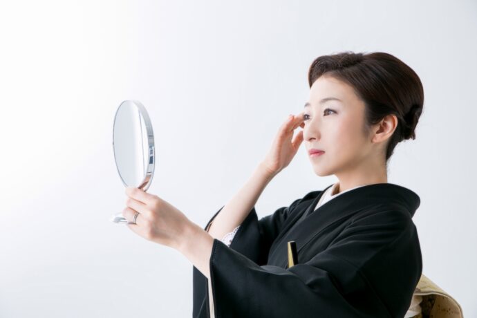 画像：手鏡で手直しをする黒留袖の女性
