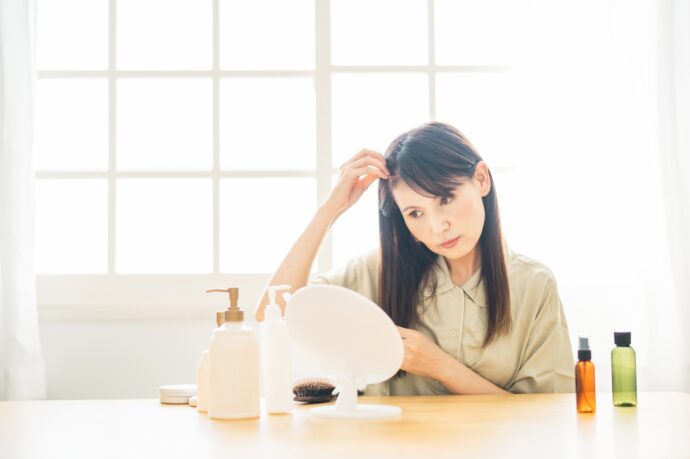 画像：鏡を見ながら髪を触るロングヘアの女性