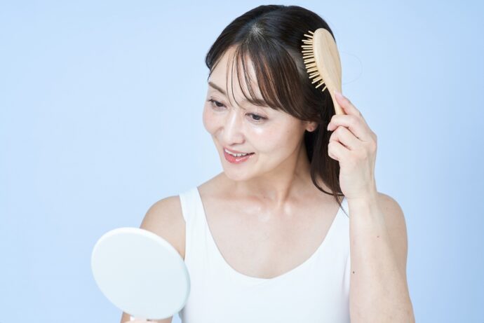 画像：鏡を見ながら髪を梳かすミディアムヘアの女性