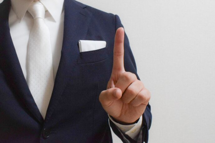 画像：人差し指を立てるスーツの男性